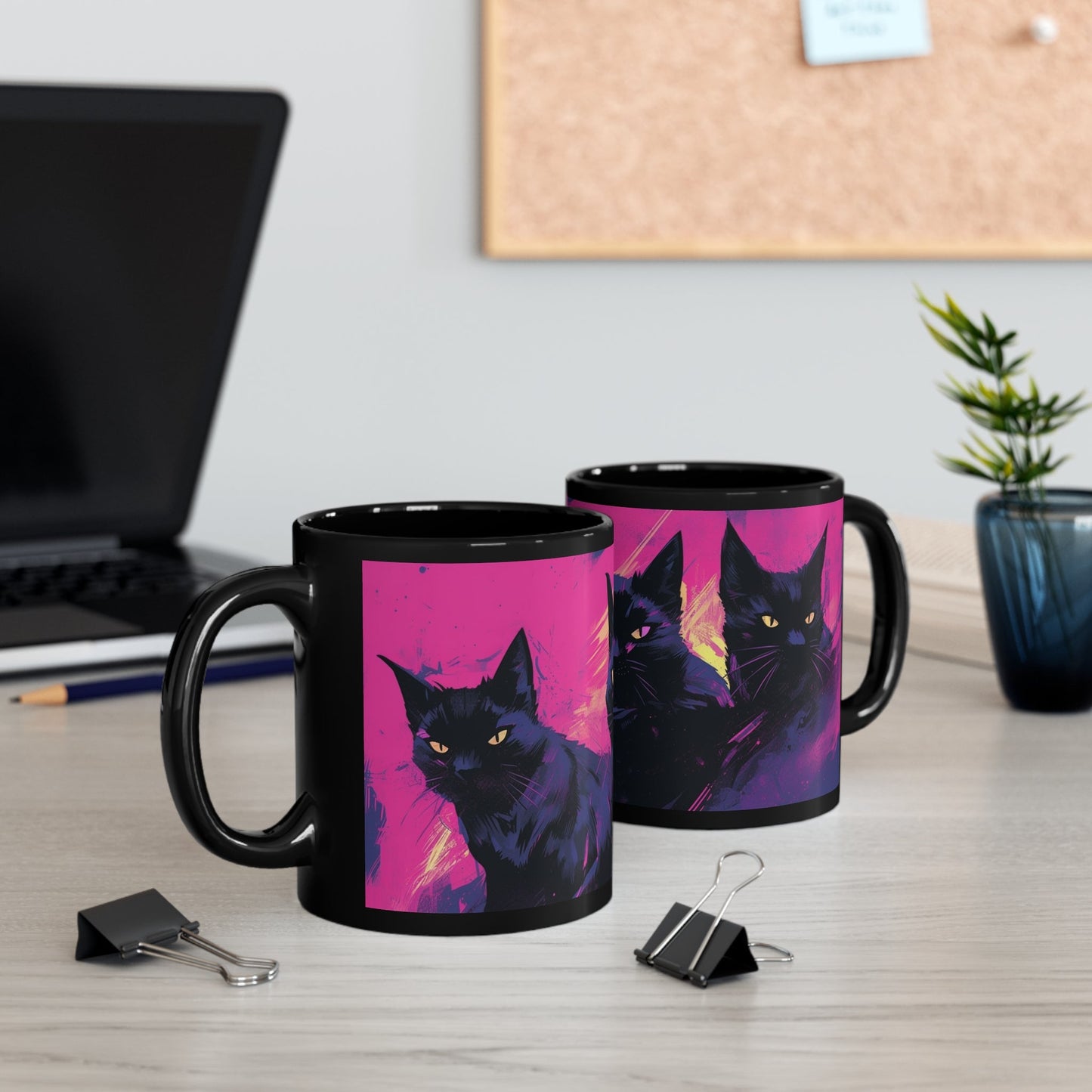 Two coffee mugs on a desk, both with an image of three black cats on a pink background painted in a watercolor style.