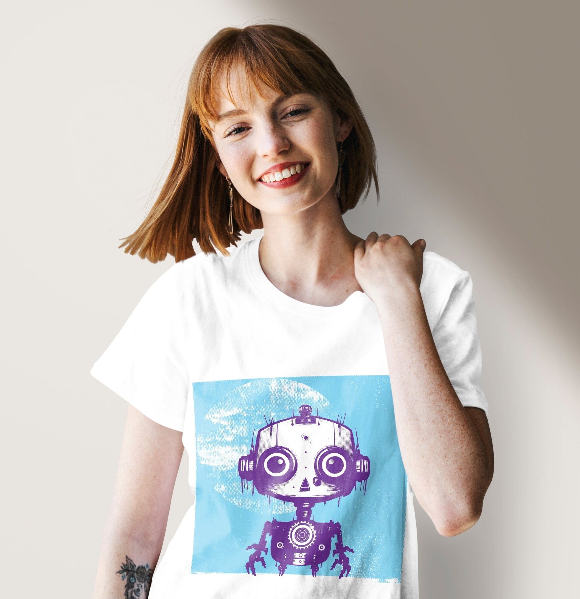 A woman wearing a white alternative fashion t-shirt with a print of a small purple robot on a blue background.