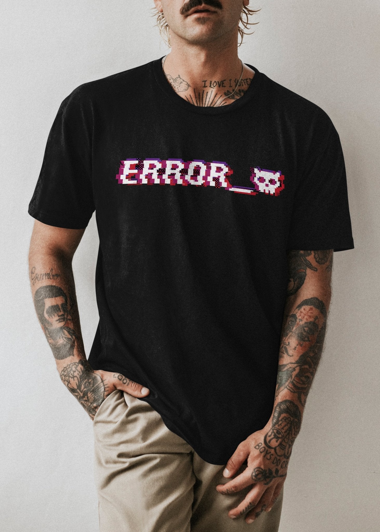 A tattooed man standing in a black alternative fashion shirt with a red and purple image of the word error along with a white pixelated devil skull next to it.